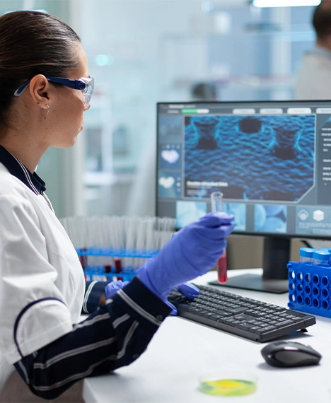 A scientist holding a vial and analyzing data on a monitor